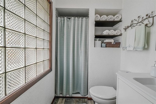 bathroom featuring toilet, a shower with shower curtain, a textured wall, vanity, and wood finished floors