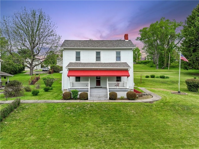 traditional-style house with covered porch, a chimney, a lawn, a shingled roof, and stairway
