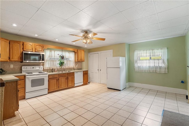 kitchen with white appliances, baseboards, a sink, backsplash, and ceiling fan