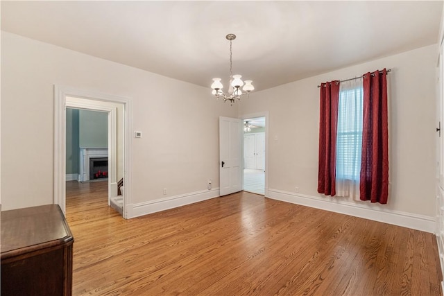 unfurnished dining area featuring a chandelier, light wood finished floors, baseboards, and a fireplace