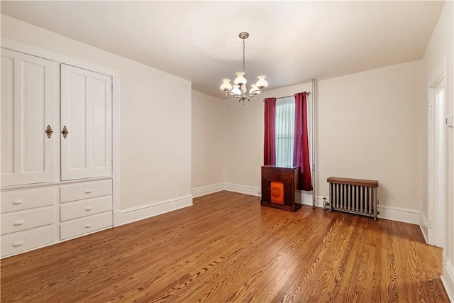 spare room featuring radiator, a chandelier, wood finished floors, and baseboards