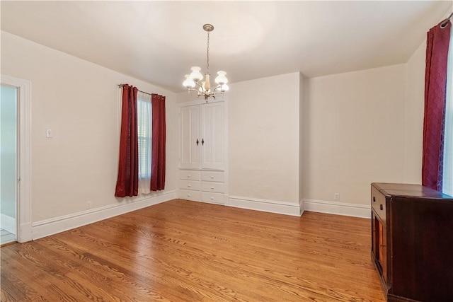 unfurnished dining area with a chandelier, light wood finished floors, and baseboards