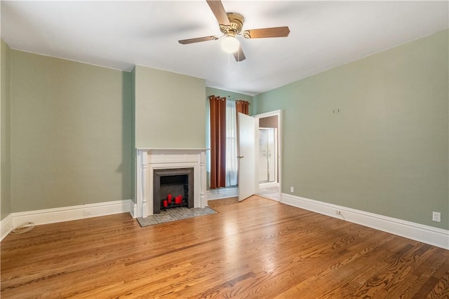 unfurnished living room featuring a ceiling fan, a fireplace with flush hearth, baseboards, and wood finished floors