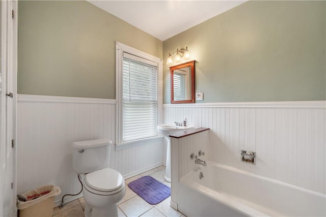 full bath featuring wainscoting, a tub to relax in, tile patterned floors, toilet, and plenty of natural light