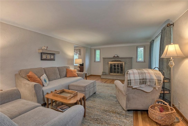 living area with wood finished floors, a brick fireplace, baseboards, and a textured wall