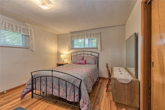bedroom featuring wood finished floors, multiple windows, a textured ceiling, baseboards, and a textured wall