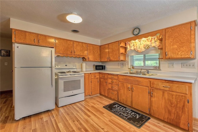 kitchen featuring white appliances, a sink, light wood-style floors, light countertops, and a textured ceiling