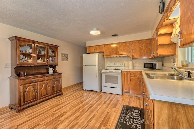 kitchen with white appliances, a sink, brown cabinetry, light wood-type flooring, and light countertops