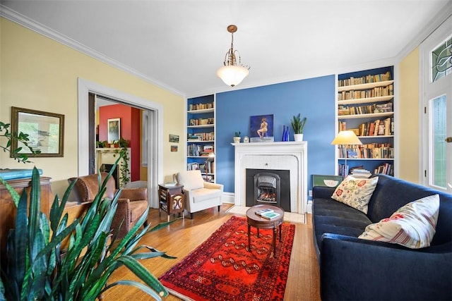 living room with built in shelves, wood finished floors, a fireplace with flush hearth, and crown molding