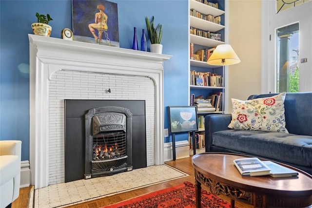 living area with wood finished floors, a fireplace with flush hearth, and built in shelves