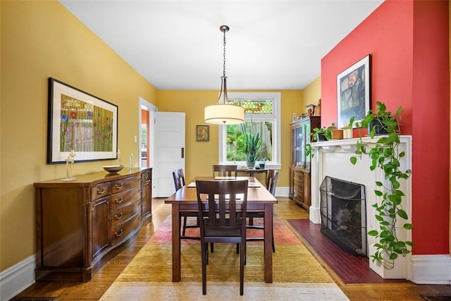 dining area featuring wood finished floors, a fireplace with flush hearth, and baseboards