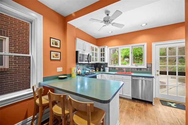 kitchen featuring stainless steel appliances, a sink, a peninsula, a breakfast bar area, and white cabinetry