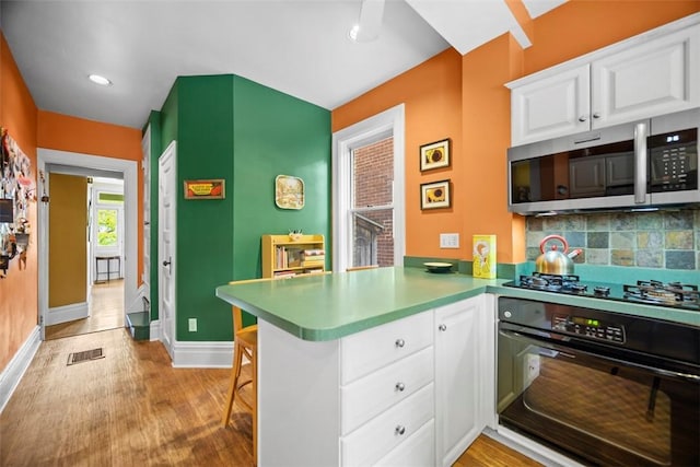 kitchen with black appliances, a peninsula, white cabinets, light wood finished floors, and recessed lighting