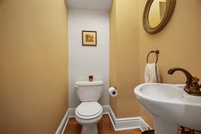 half bath with a sink, baseboards, toilet, and wood finished floors