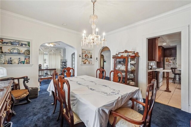 dining room with arched walkways, a chandelier, ornamental molding, dark colored carpet, and dark tile patterned floors