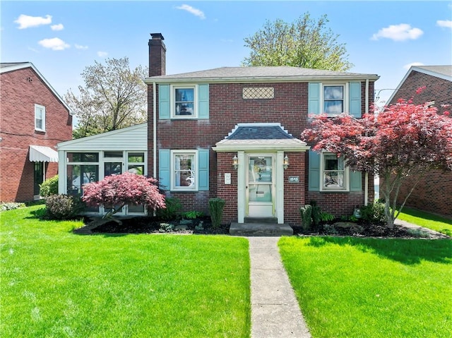 view of front facade featuring a chimney, a front yard, and brick siding