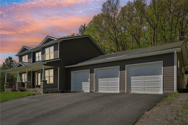 view of front of house featuring asphalt driveway, covered porch, a garage, and metal roof