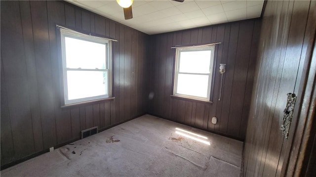 unfurnished room featuring ceiling fan, carpet floors, and wooden walls