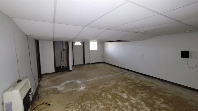below grade area with heating unit, a drop ceiling, and baseboards