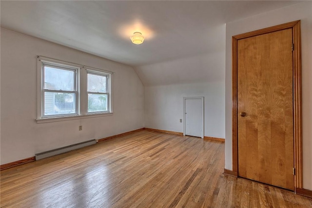 additional living space with a baseboard radiator, wood finished floors, vaulted ceiling, and baseboards