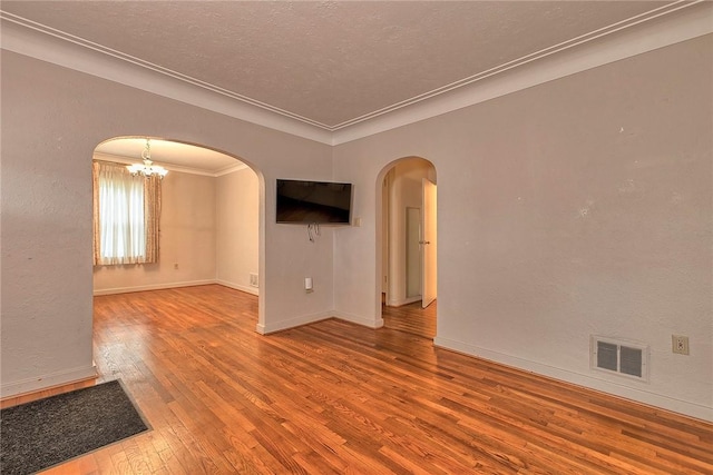 unfurnished room featuring arched walkways, hardwood / wood-style flooring, ornamental molding, baseboards, and a textured ceiling