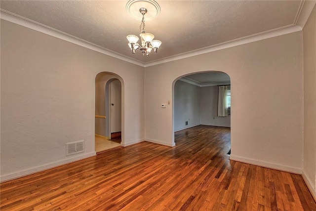spare room with arched walkways, a chandelier, hardwood / wood-style flooring, ornamental molding, and baseboards