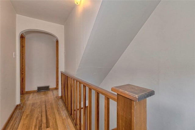 hallway with light wood-style flooring, arched walkways, and baseboards