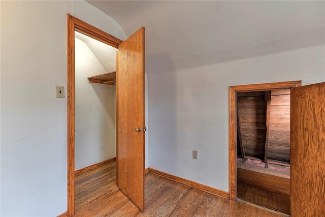 unfurnished bedroom with wood finished floors, vaulted ceiling, a closet, and baseboards