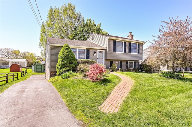 split level home with a storage unit, a chimney, an outdoor structure, and asphalt driveway