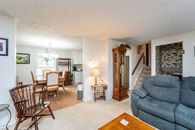 living room featuring a chandelier, a textured ceiling, stairs, baseboards, and light colored carpet