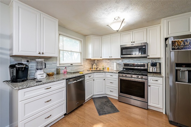 kitchen featuring appliances with stainless steel finishes, a sink, white cabinets, decorative backsplash, and a textured ceiling