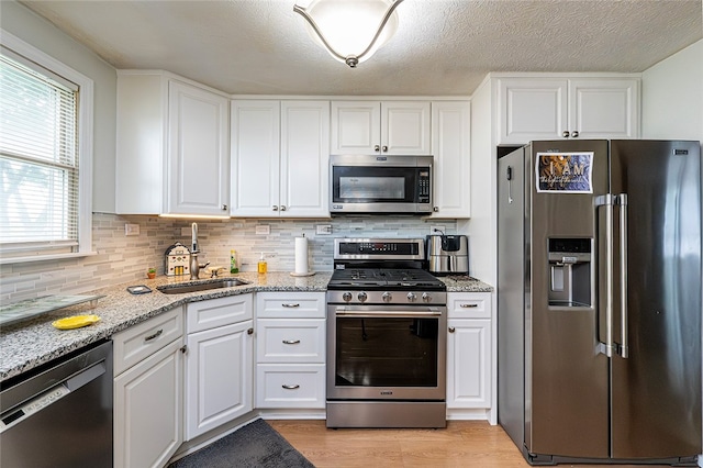 kitchen with appliances with stainless steel finishes, a sink, white cabinets, and a textured ceiling