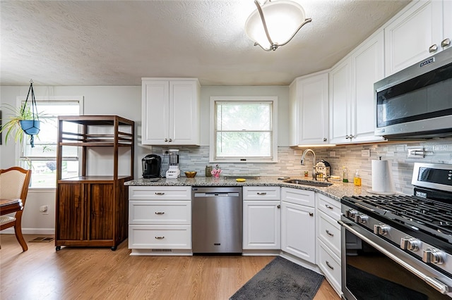 kitchen featuring appliances with stainless steel finishes, a sink, light wood-style flooring, a textured ceiling, and backsplash