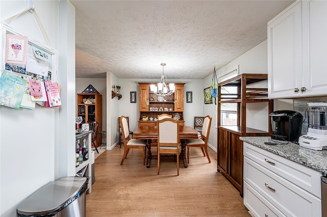 dining space featuring a chandelier, light wood finished floors, baseboards, and a textured ceiling