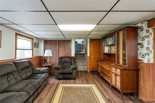 living room with a drop ceiling, wood walls, wood finished floors, wainscoting, and stairway