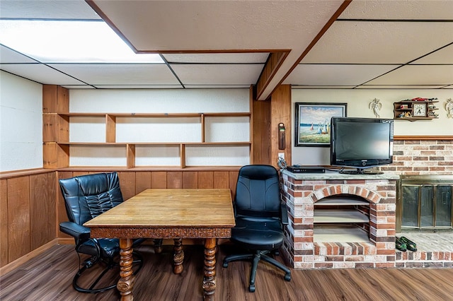 office featuring wood finished floors, a paneled ceiling, wood walls, and a brick fireplace