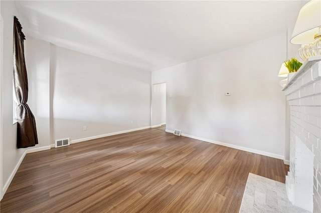 unfurnished living room with wood finished floors, baseboards, and a brick fireplace