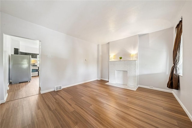 unfurnished living room featuring wood finished floors, baseboards, and a brick fireplace