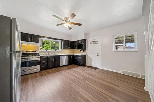 kitchen featuring appliances with stainless steel finishes, a ceiling fan, light countertops, under cabinet range hood, and wood finished floors