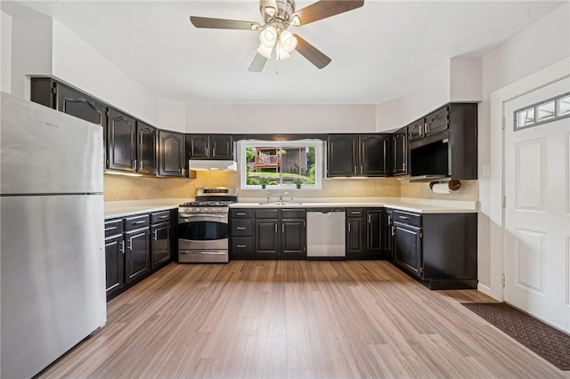 kitchen with appliances with stainless steel finishes, under cabinet range hood, a sink, light wood-style flooring, and light countertops