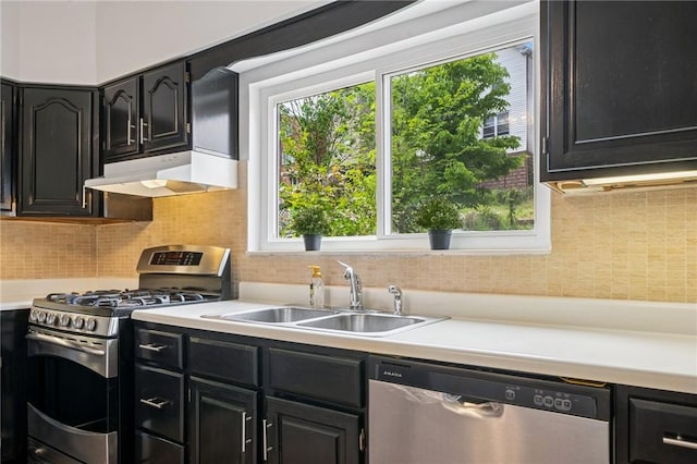 kitchen with appliances with stainless steel finishes, under cabinet range hood, a sink, dark cabinets, and light countertops