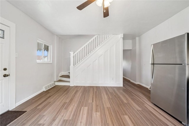unfurnished living room with wood finished floors, stairs, a ceiling fan, and baseboards