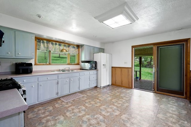 kitchen featuring white fridge with ice dispenser, a sink, a textured ceiling, a wainscoted wall, and light countertops