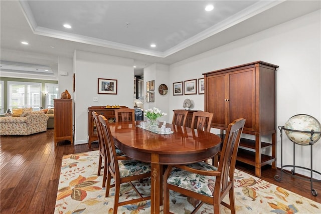 dining space with wood-type flooring, recessed lighting, a tray ceiling, crown molding, and baseboards
