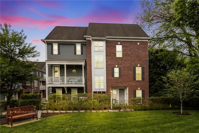 view of front of home with a yard, a balcony, roof with shingles, and brick siding