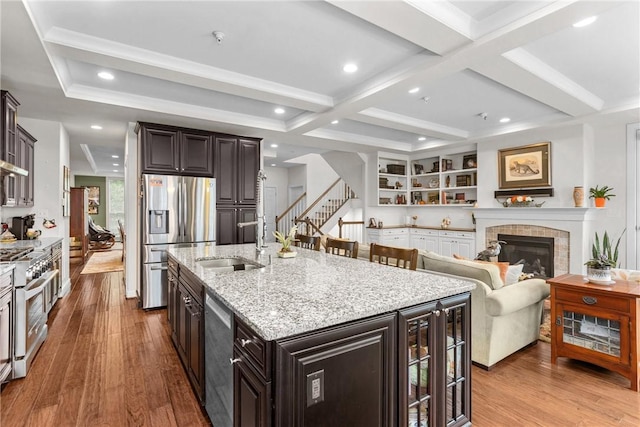 kitchen featuring stainless steel appliances, a sink, wood finished floors, light stone countertops, and beamed ceiling
