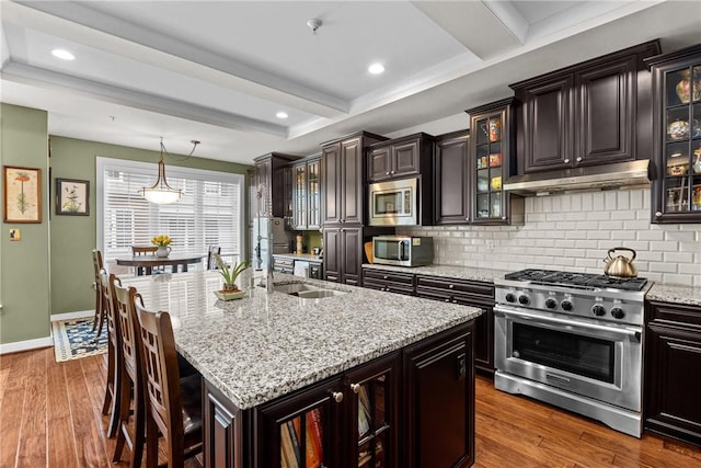 kitchen featuring stainless steel appliances, under cabinet range hood, a sink, decorative backsplash, and beam ceiling