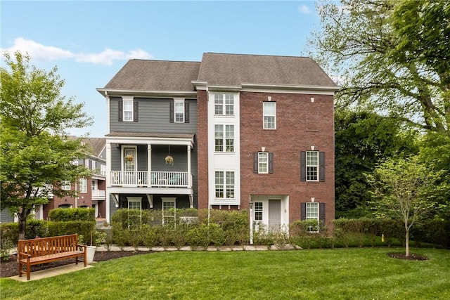 back of property featuring a yard, roof with shingles, brick siding, and a balcony