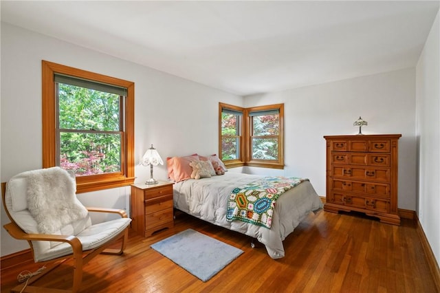 bedroom with multiple windows, wood-type flooring, and baseboards