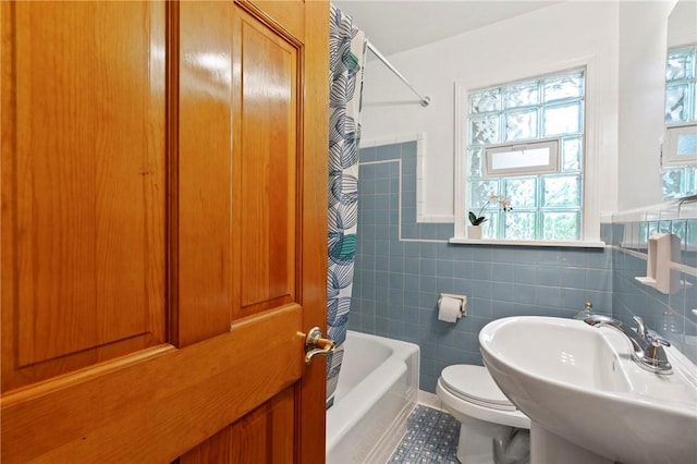 bathroom featuring toilet, a sink, tile walls, shower / bath combo with shower curtain, and tile patterned flooring